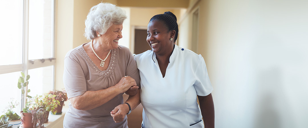 Nurse and resident walking arm and arm down a bright hallway